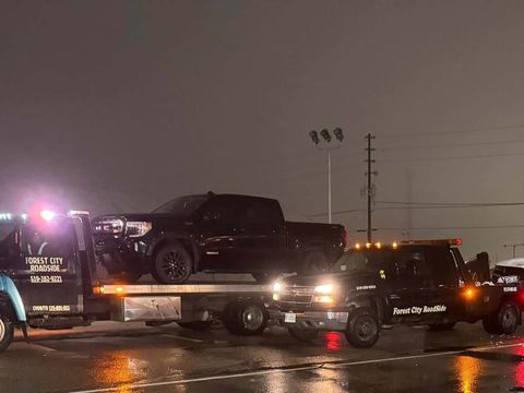 Forest City Roadside flatbed and wrecker trucks recovering vehicles at night on a wet road