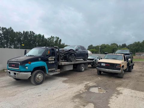 Two Forest City Roadside flatbed tow trucks loaded with vehicles in a yard near London Ontario